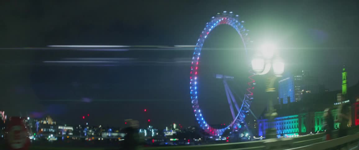 Distant illuminated ferris wheel seen from a moving car at night