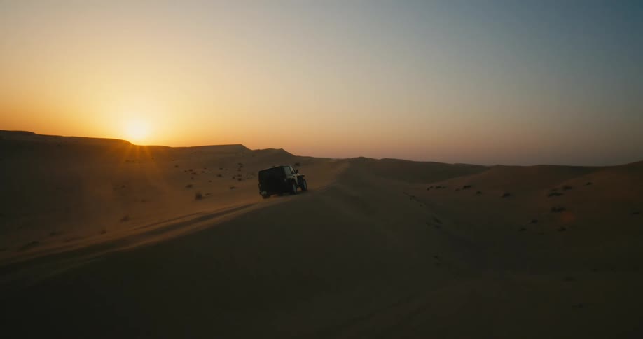 A jeep drives down a sand dune