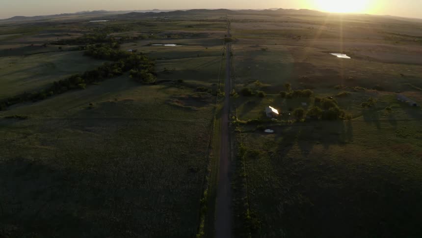 Sun shines from horizon on house and highway passing countryside
