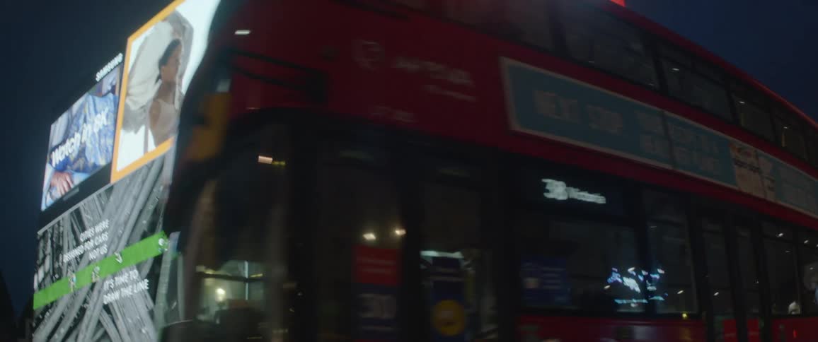 A doubledecker city bus enters a downtown intersection with video billboards at night