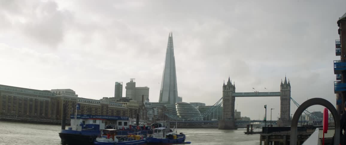 Boats are in a harbor and buildings are on the other side of the river under a cloudy sky