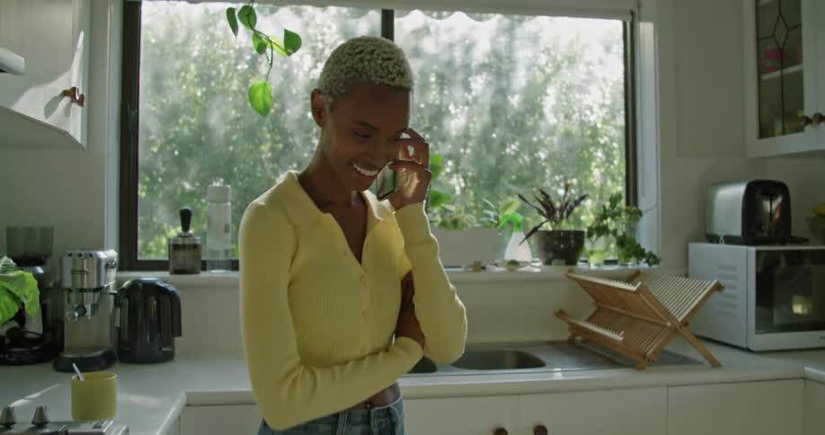 A woman is walking and talking on a smartphone in a home kitchen during the day