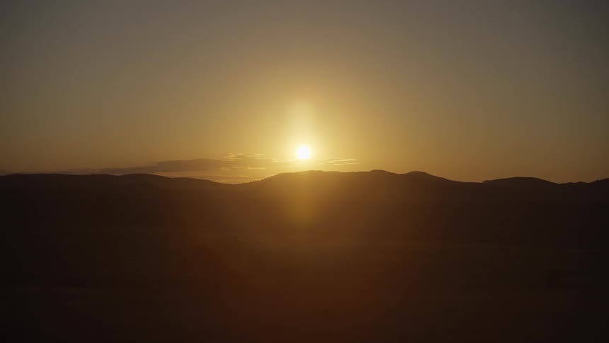 The sun is setting over a silhouetted mountain ridge