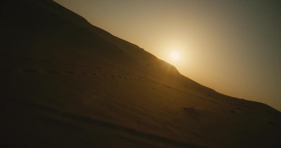 An aerial view of the sun setting over sand dunes in a remote desert