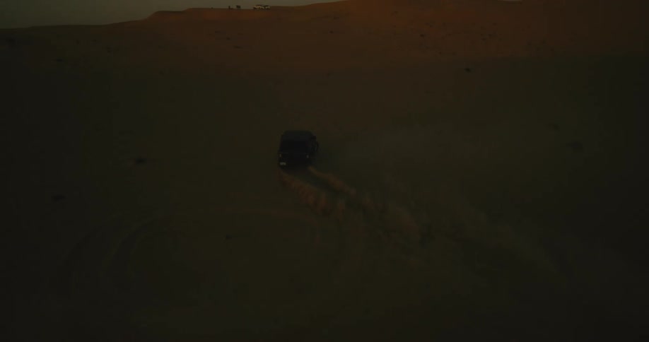 A vehicle kicks up a cloud of sand while making a sharp turn off road in the desert in the evening