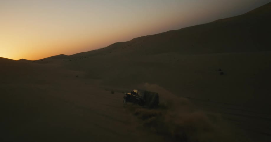 A black jeep travels across a desert as sand flies through the air