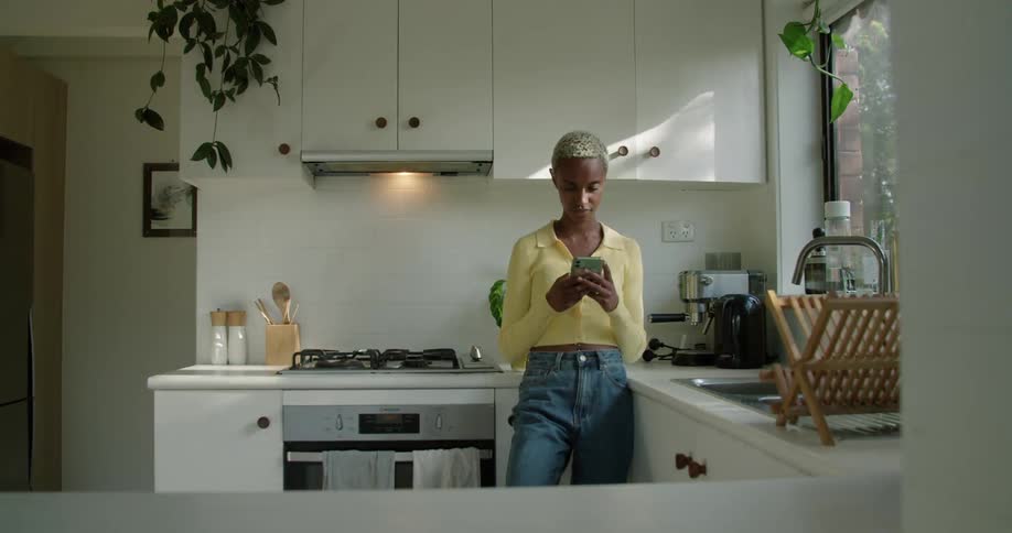 A woman stands in a kitchen using a smartphone