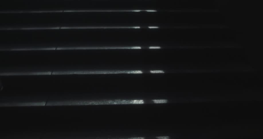 Shadows of people walking near dark stairs illuminated by slivers of light