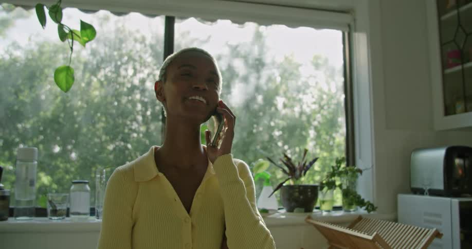 A woman is standing in a kitchen talking on a cell phone