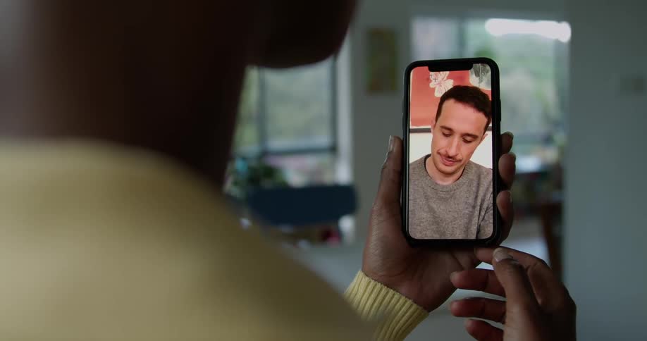 Woman with short hair and yellow sweater holds smartphone and makes a video call in living room