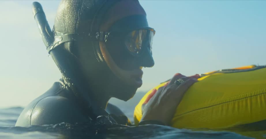 A man wearing a wet suit and snorkel mask treads water while holding onto a yellow raft