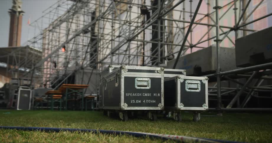 Two crates on grass with scaffolding the sky and clouds in the background