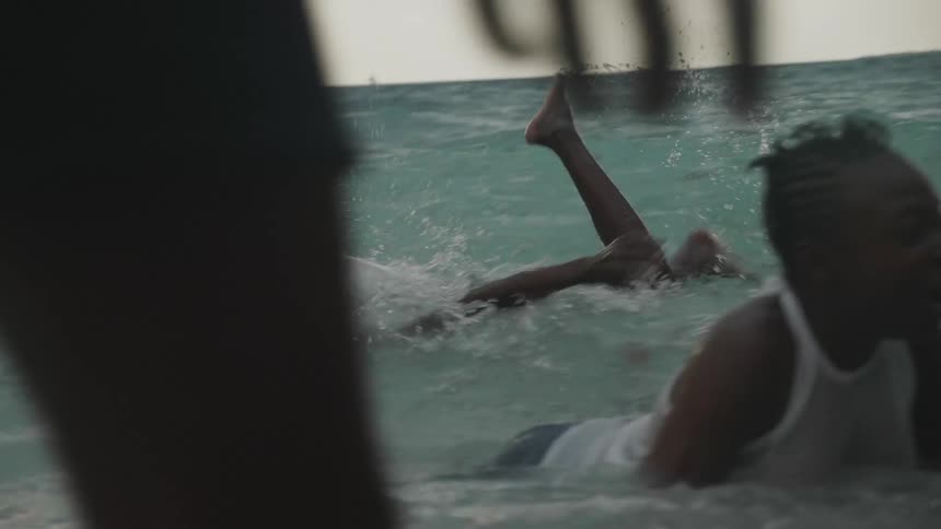 Children are floating and swimming in an ocean near a tropical beach on an overcast day