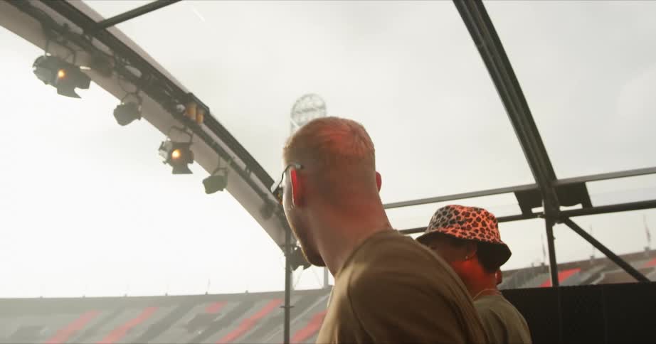 Two men on a stage in a stadium with the sky and clouds in the background