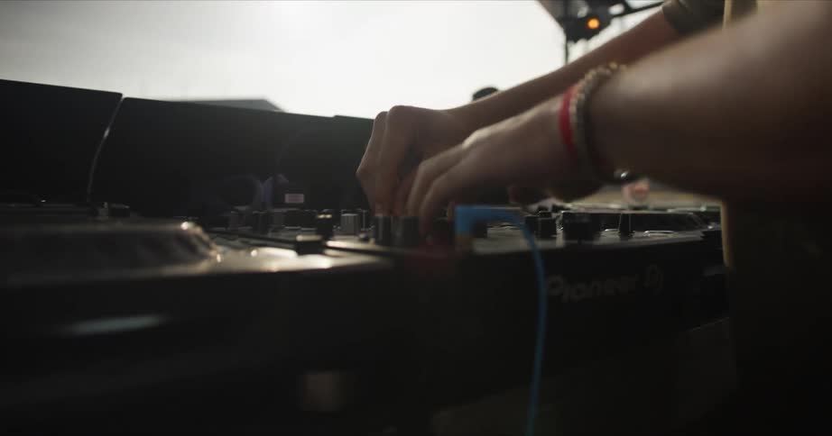 A man disc jockeying turning knobs and dancing on a stage with the sky and clouds in the background