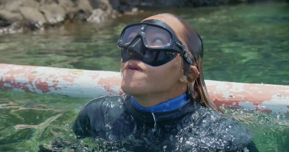 A female diver wearing a snorkel mask and wet suit is coming up out of water