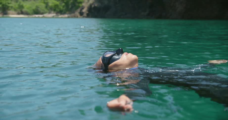 A female diver is wearing goggles and floating on the surface of ocean water