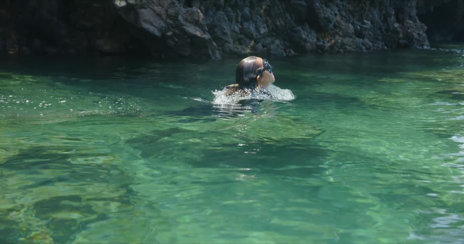 A female diver wearing snorkel gear is coming up out of the water in the ocean