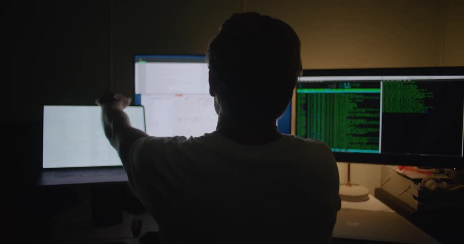 A man sitting at a desk stretches then closes his laptop and stands up