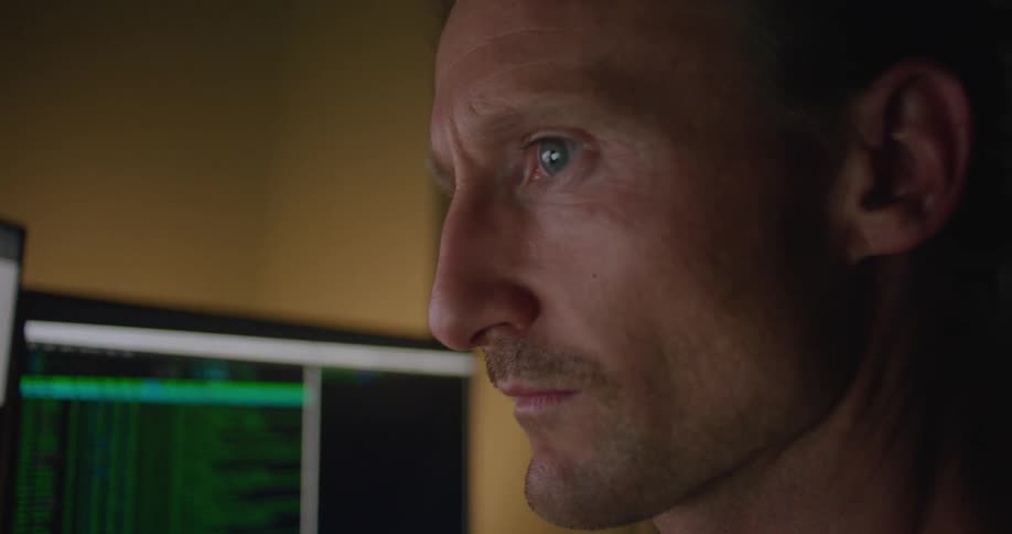 A man stares at data scrolling on multiple monitors