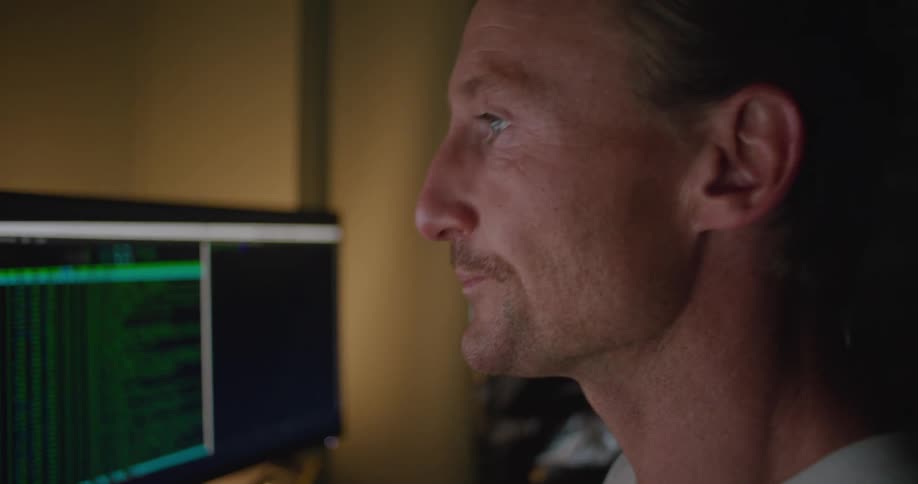 A man rubs his face while looking at computer screens