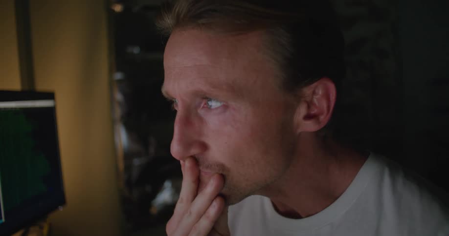 A man rubs his face while watching the computer monitors
