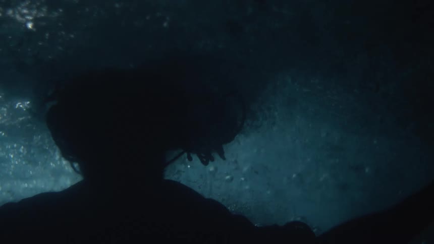 Underwater footage of a still body of water as a woman swims to the surface