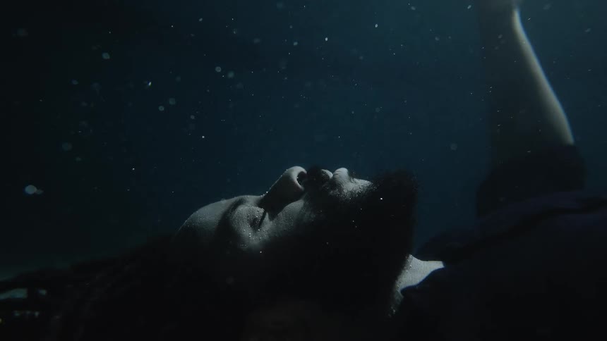 Man with braided hair and beard goes underwater with eyes closed
