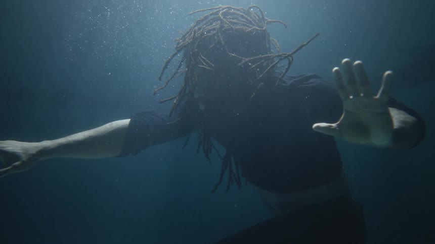 A man stands under water and stretches his arms and moves them around his body
