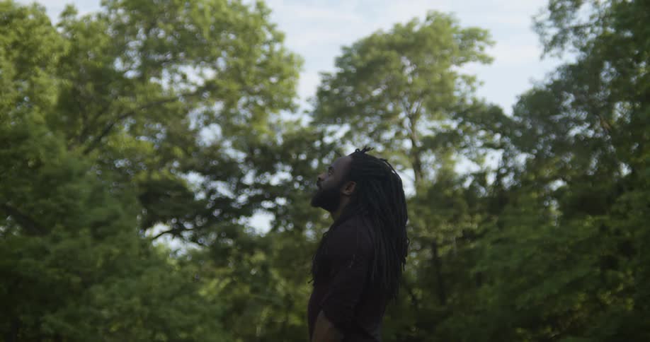 A man standing outside with trees the sky and clouds in the background