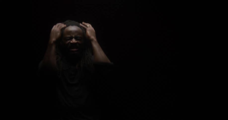 A man clutches his head in agony and despair as a spot light flickers and strobes