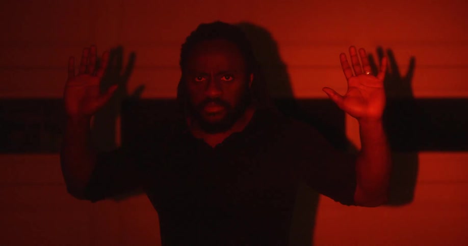 Man with braided hair beard and black shirt surrenders to police with hands up in flashing colored lights