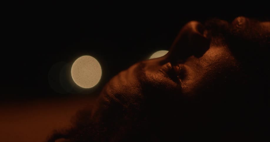 A man looks up at the ceiling while lying in a dark room