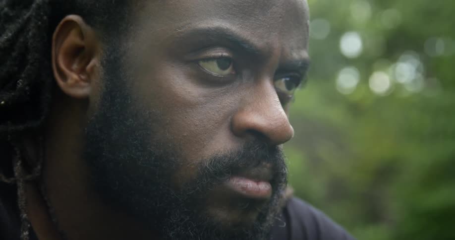 Angry man with braided hair and beard looks around in the forest
