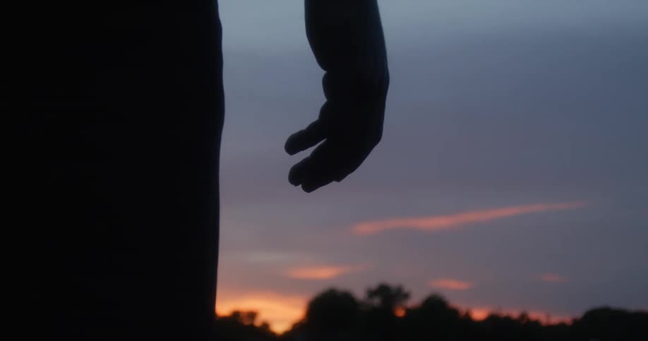 Silhouette of a person standing outside watching the sun set on a cloudy day at dusk