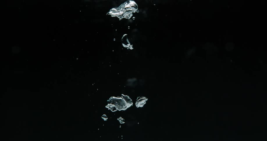 Clear bubbles rise up and break apart in liquid against a black background