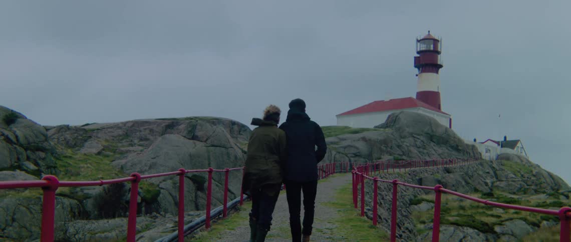 Couple wearing coats walk up walkway toward lighthouse