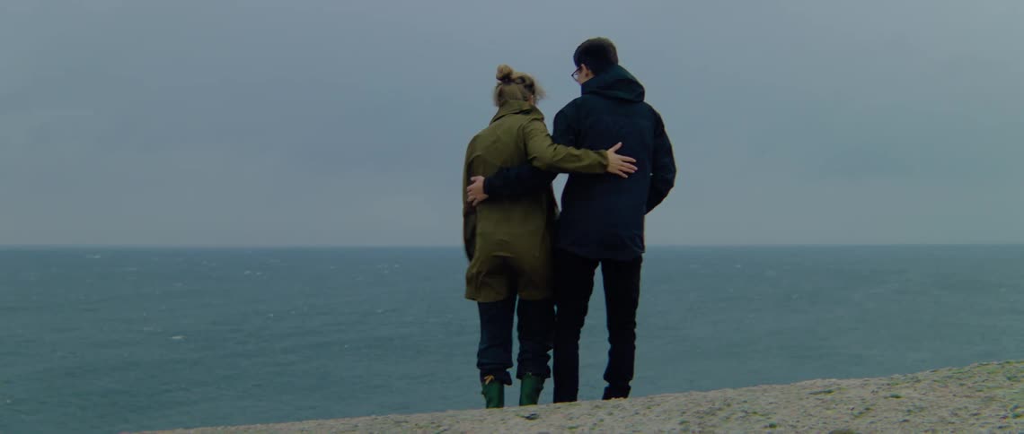 A man and woman are kissing and hugging as they look over the water