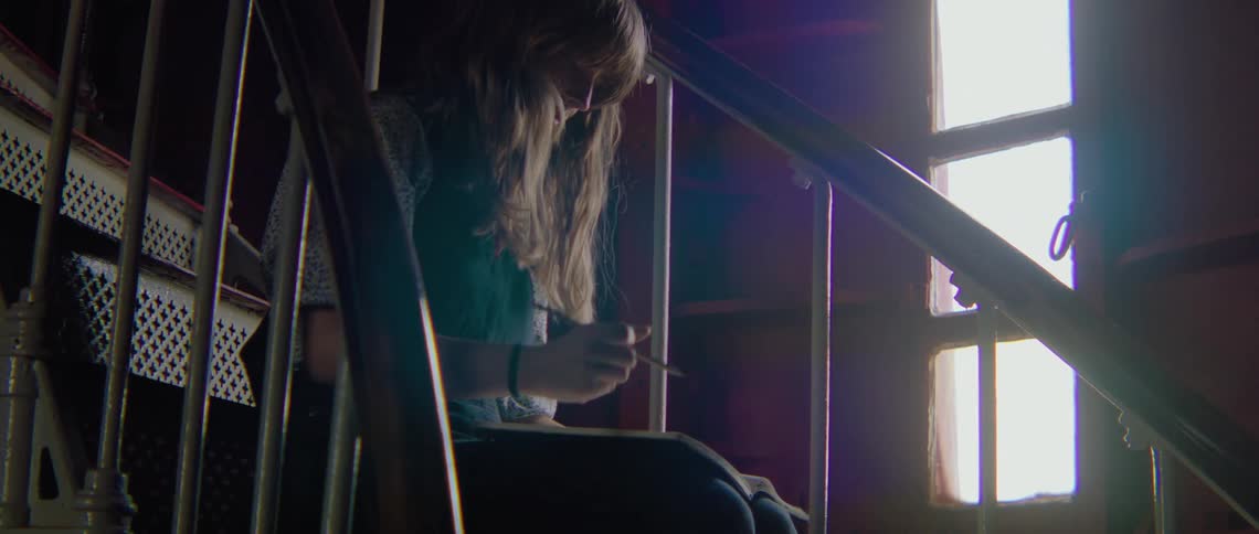 A woman sitting on a staircase with a pencil and a book with a wall and window in the background