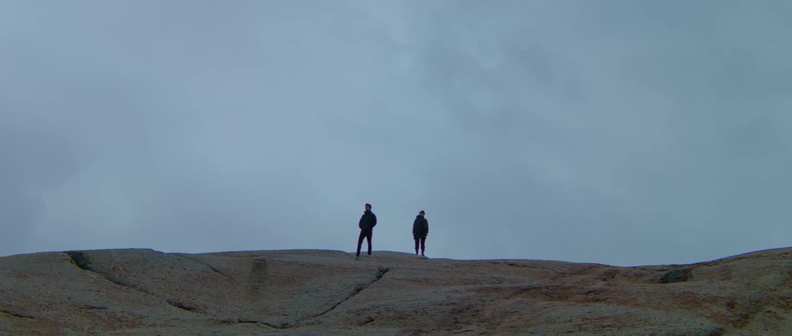 Two men stand on top of a sand dune at dusk