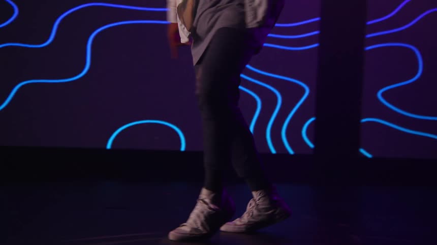 A man dances hip hop style in front of a large screen with digital graphics