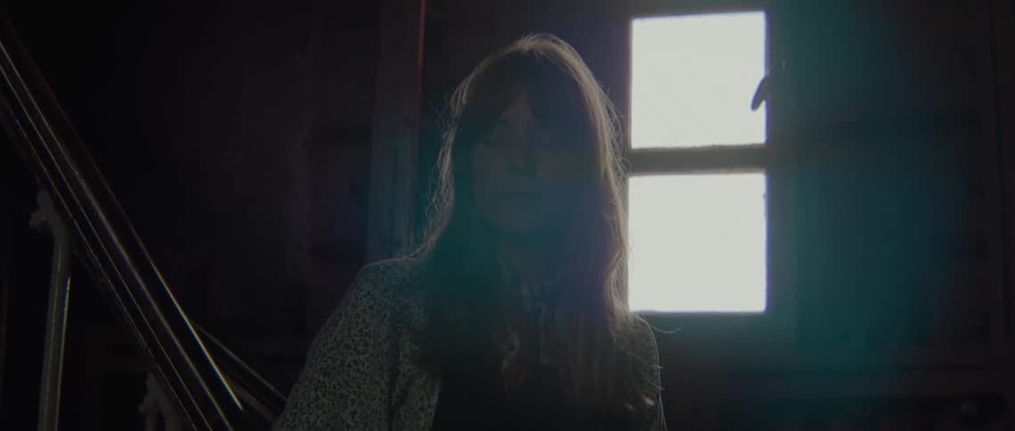 A woman in a room with a staircase a wall and a window in the background