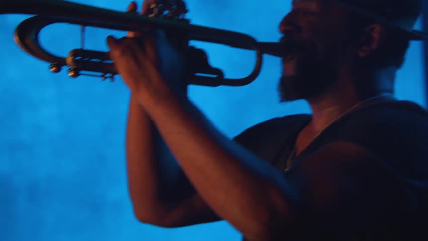A black man wearing a hat is playing a trumpet