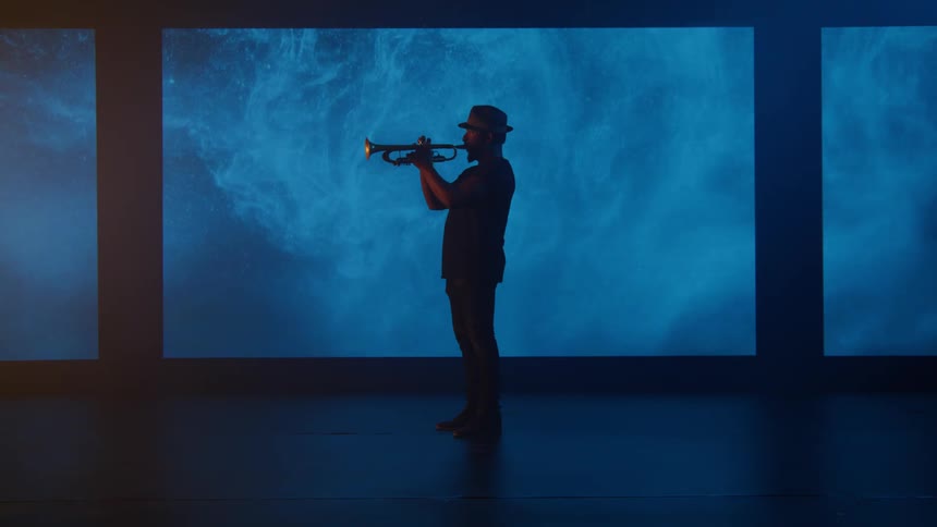 A man wearing dark clothes and a hat is playing a trumpet