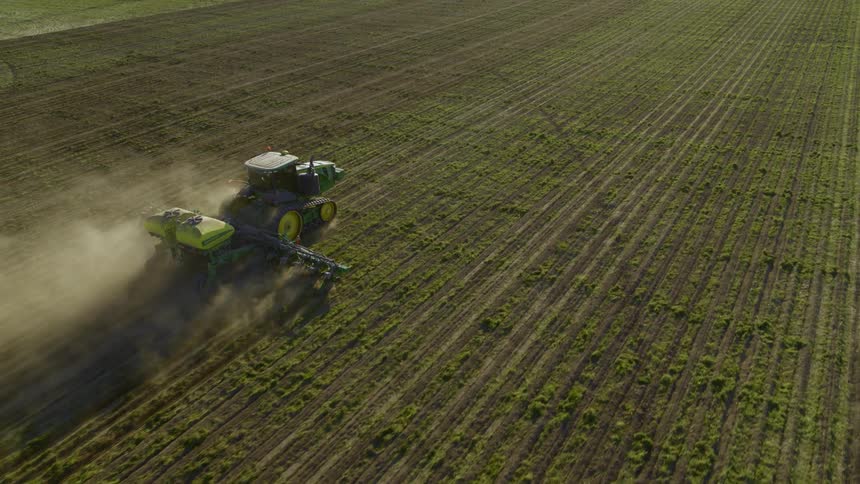 A tractor tills the soil on farmland while leaving a trail of dust