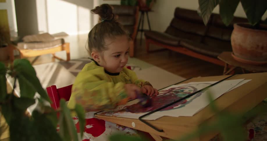 A little girl is painting at a table in a living room during the daytime