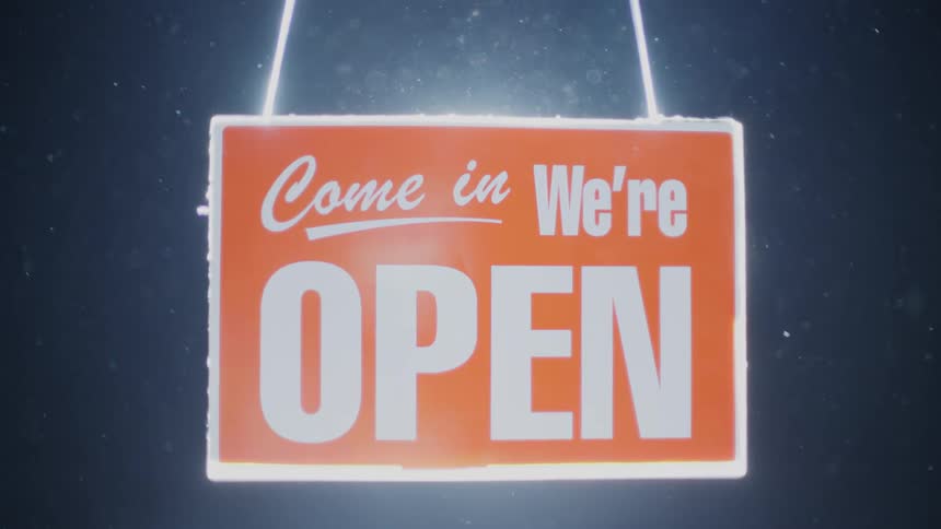 An open sign glows as the light shining on it fades on a snowy night
