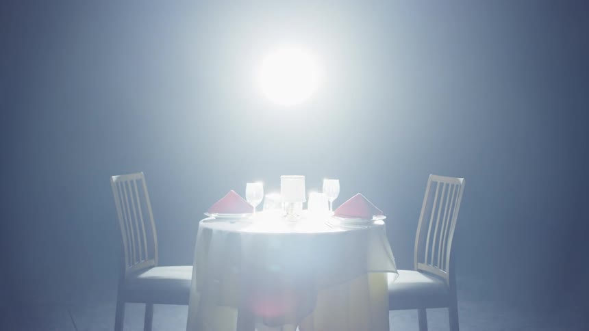 Table with white tablecloth plates and glasses in the spotlight