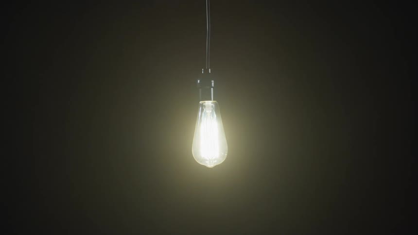 A bright lightbulb hanging from the ceiling is lit in the darkness