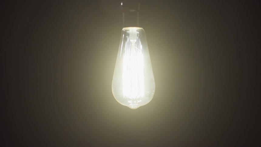 A lightbulb hanging from the ceiling lights up in the darkness